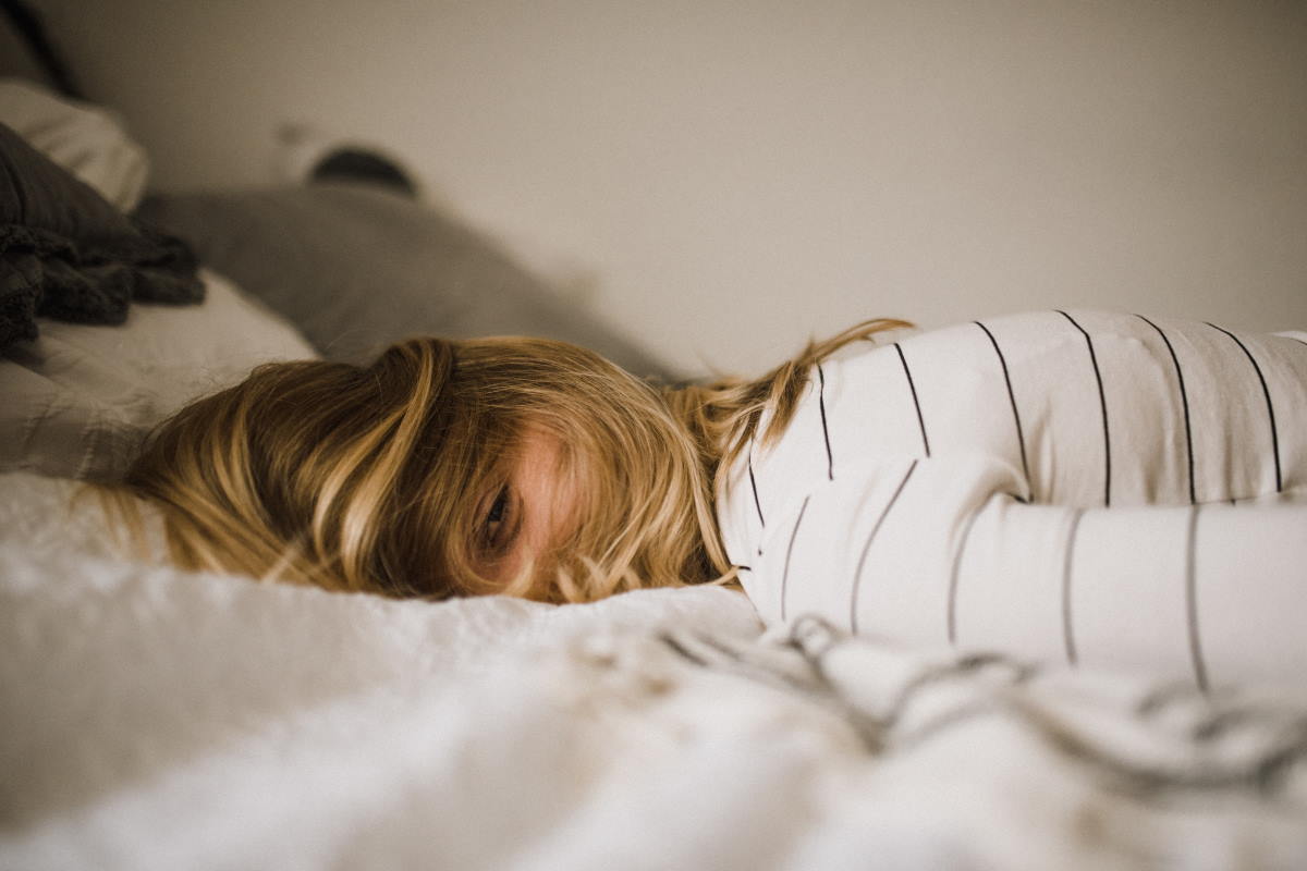 Blonde woman lying down on bed with her hair covering most of her face