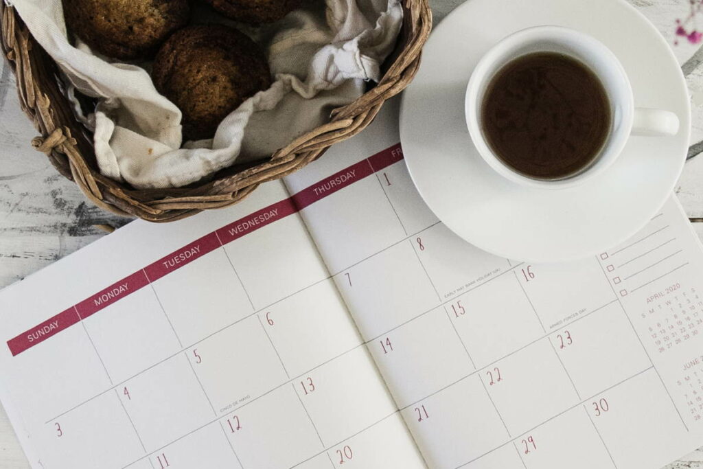 Cup of tea on a saucer next to a calendar and basket of cakes
