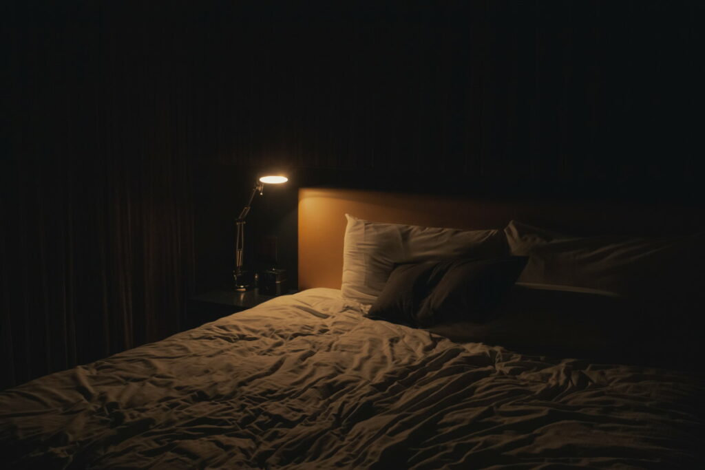 Dark bedroom with a lamp shining on the bedside table