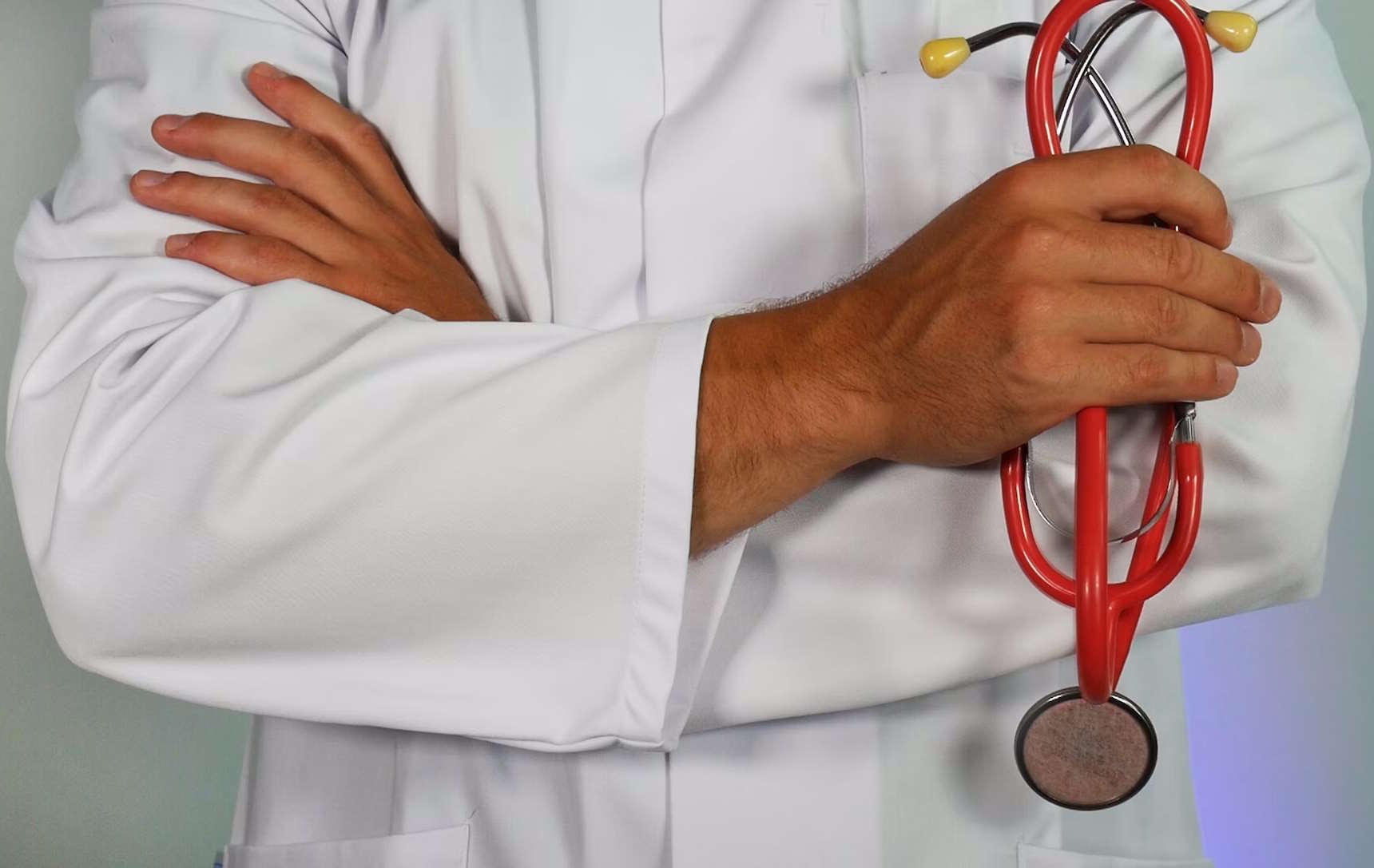 Torso of a doctor in a white lab coat with their arms folded, holding a stethoscope in one hand