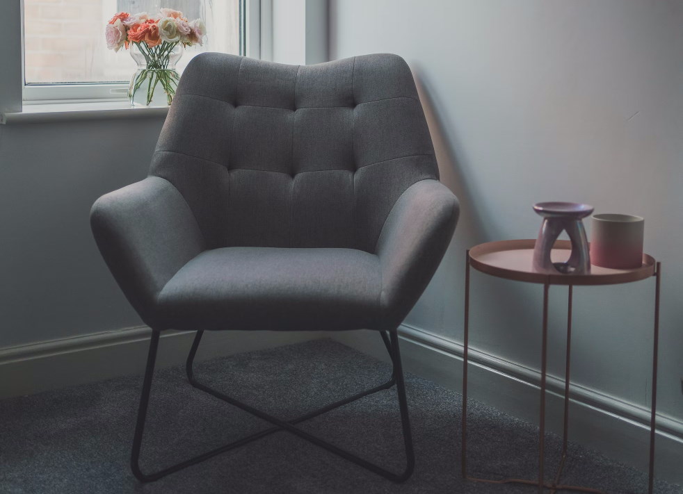 Grey modern armchair next to small table with vase on