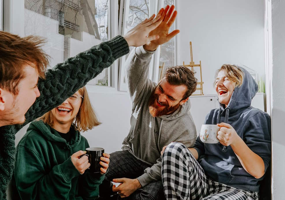 Group of 4 people sat together and laughing. Two of them are high-fiving. 