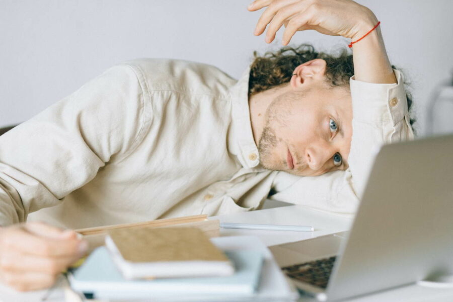 Frustrated man slumped on a desk in front of a laptop