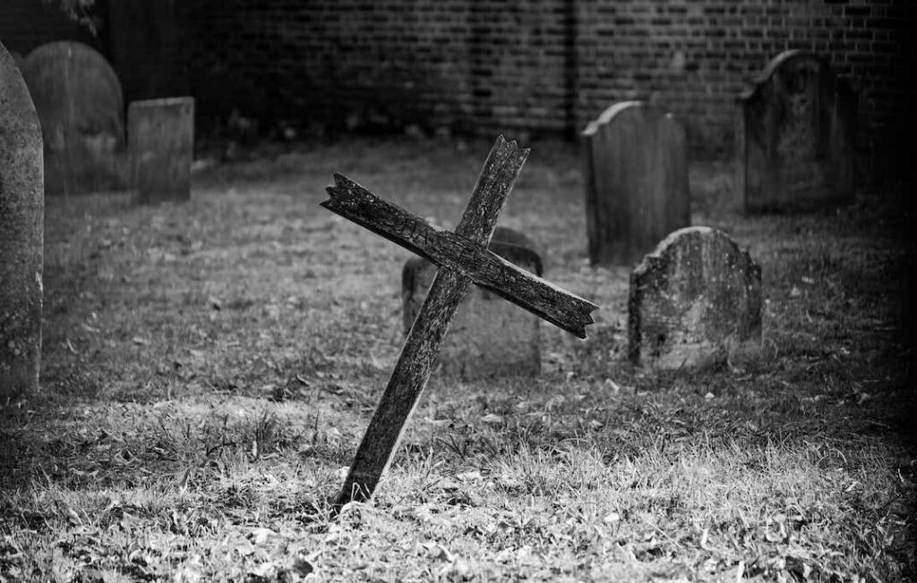Black and white image of a graveyard with a wonky cross in the foreground