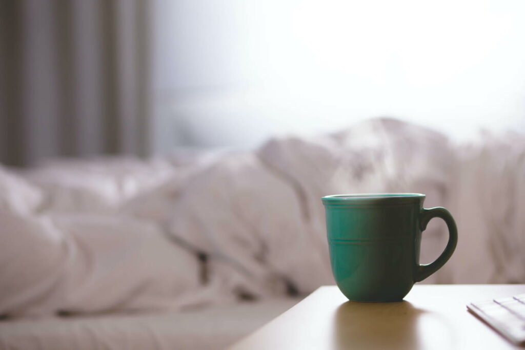 A green ceramic mug on top of a wooden table with a bed in the background