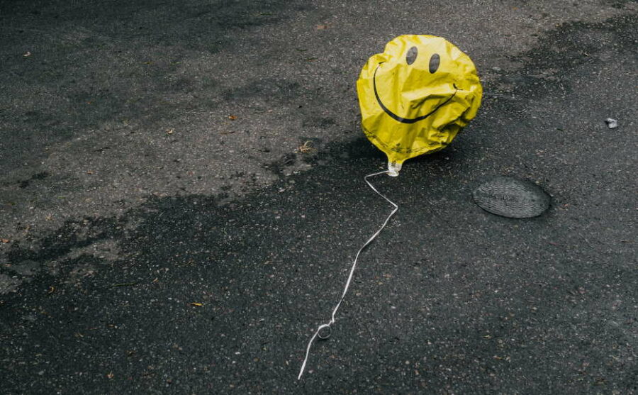 Crumpled yellow balloon with a smiley face on it lying on the road