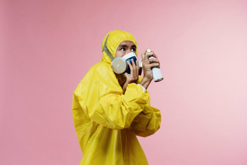 Man looking afraid wearing a hazmat suit and a gas mask while holding an aerosol can