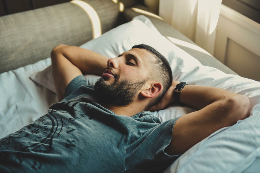Man sleeping on a bed with his arms behind his head