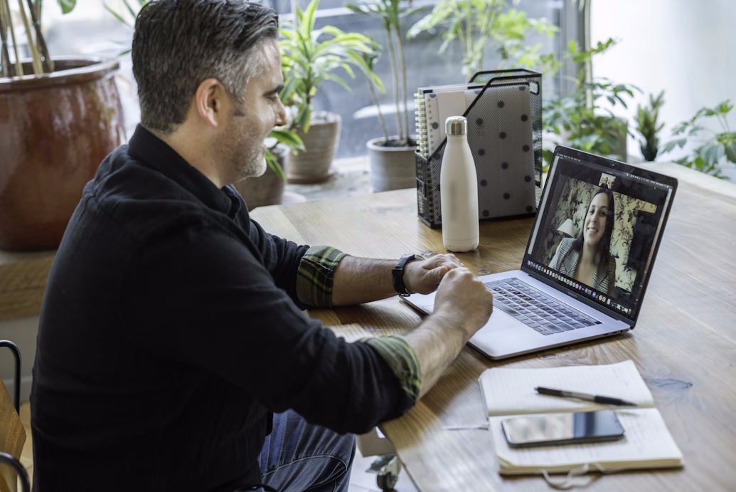 Man sat at desk on a Zoom call with a woman on his laptop.