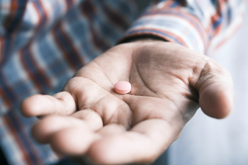 Man holding a pink round pill in the middle of his palm
