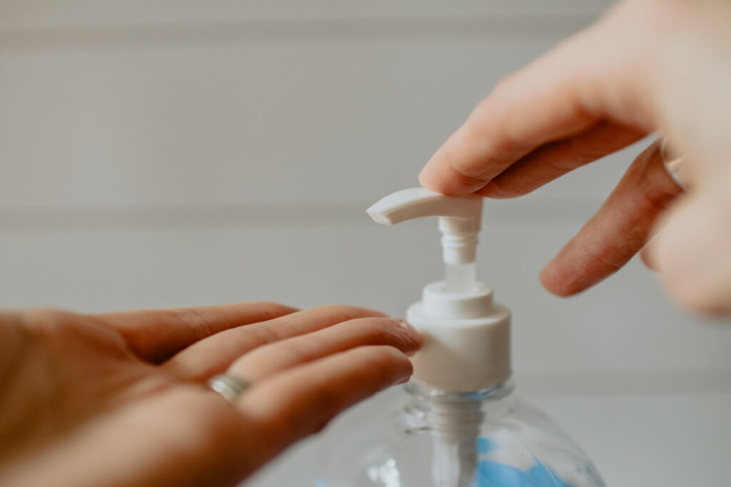 One hand pressing down on the pump of a bottle of hand sanitiser, with another hand below the pump