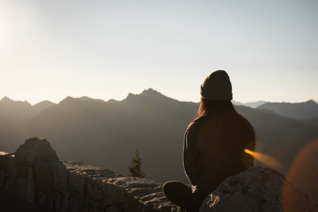 Person wearing a hat sitting down facing mountains