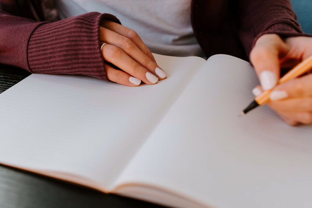 Close up of a person in a red sweatshirt holding a pen above a blank page of a journal.
