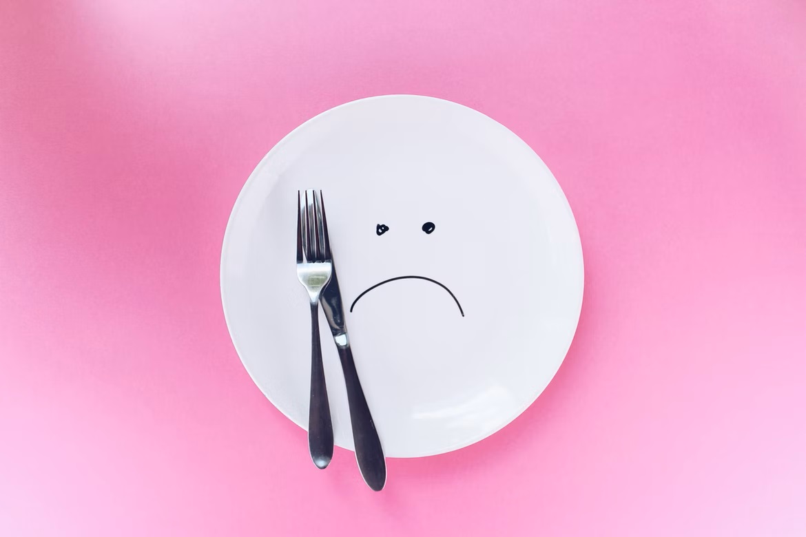 White plate with sad face and knife and fork on top of it