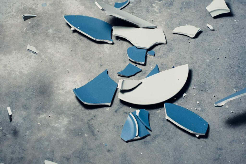 A blue plate that has smashed to pieces on a concrete floor
