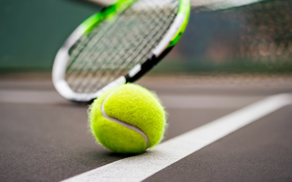 close up of a tennis ball on a court with a racket visible in the background