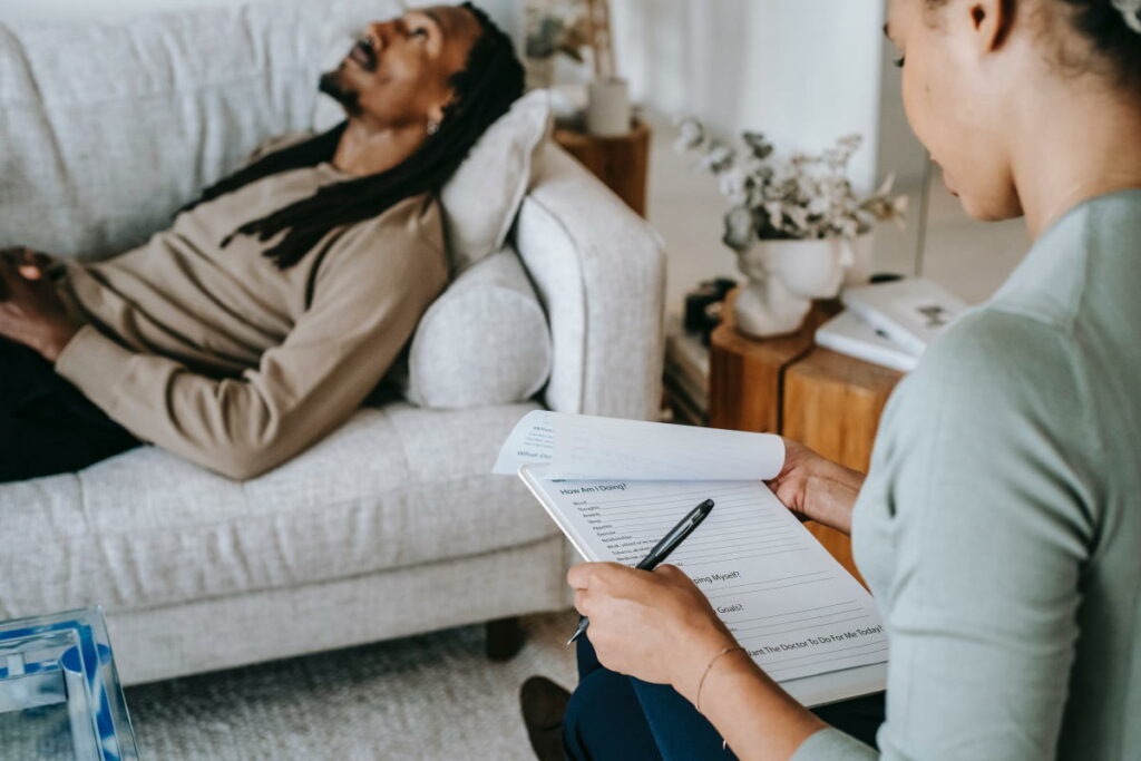 Therapist looking at a form while a male patient lies on a sofa in the background