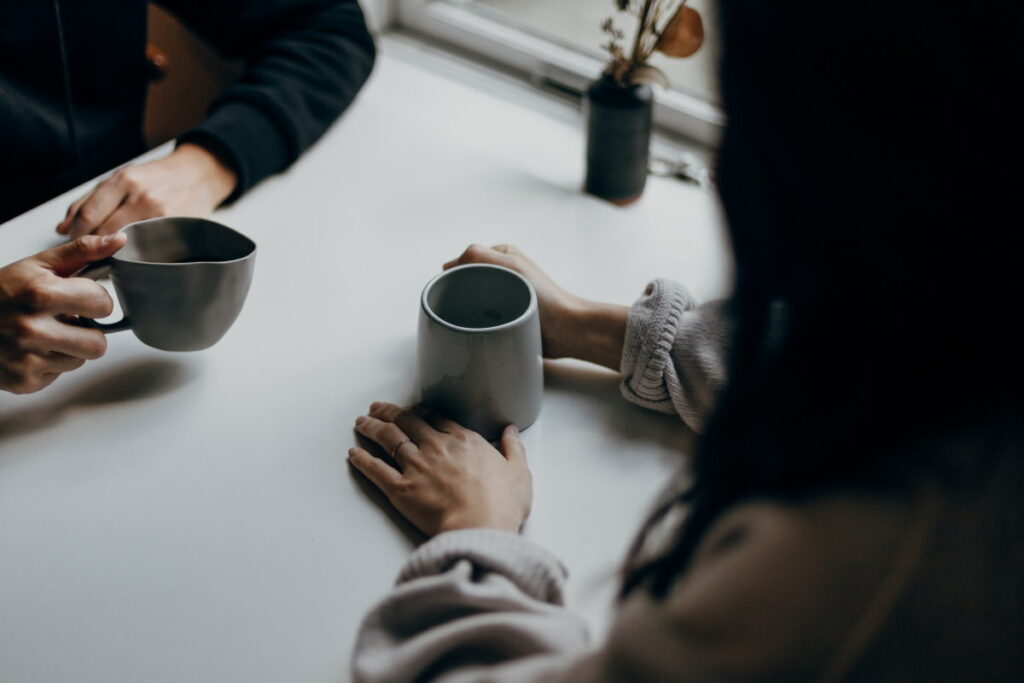 Two women sitting at a table holding cups of coffee