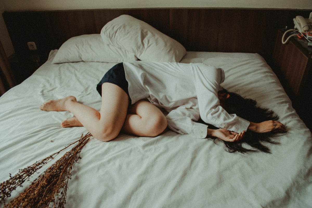 Woman curled up on bed with white sheets