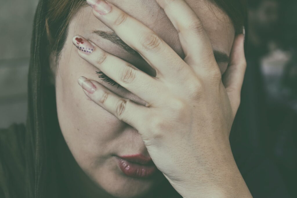 A woman holding her hand over her face with her eyes closed