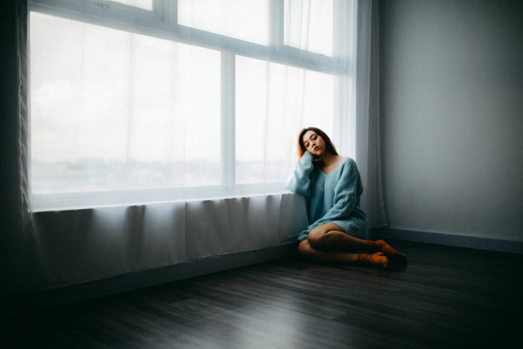 Woman in a blue jumper sat on the floor next to a window