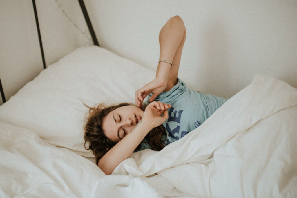 Woman stretching her arms in a bed with white covers