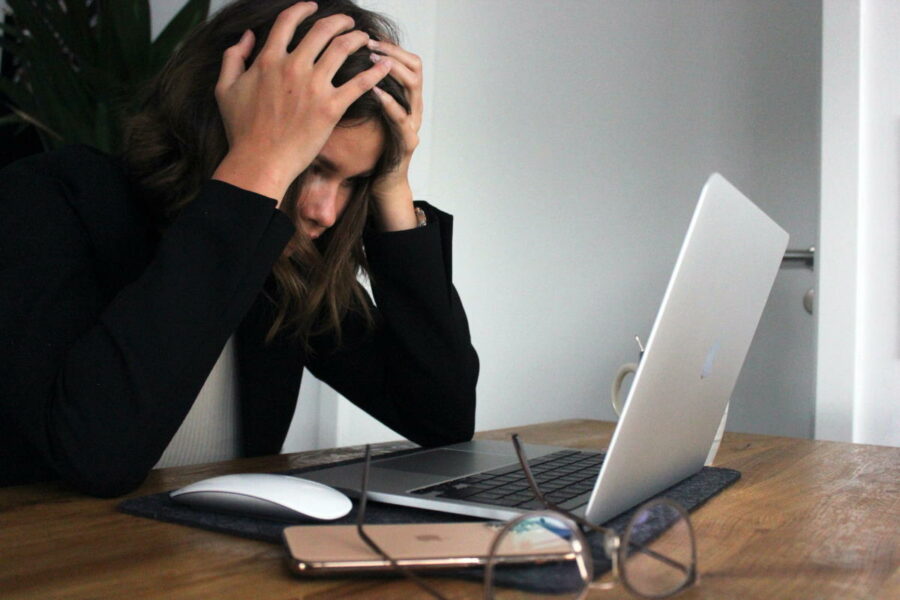 Woman in black shirt holding her head while staring at laptop